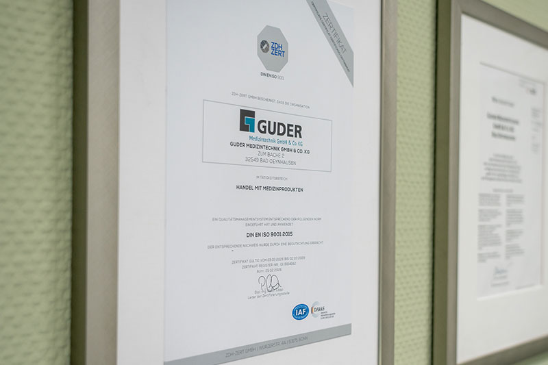 Die gerahmte Urkunde an der Wand bestätigt, dass die Guder Medizintechnik GmbH & Co. KG über ein kundenorientiertes Qualitätsmanagementsystem verfügt.